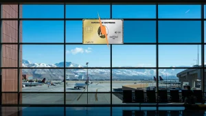 Eine American Express Karte zur Hälfte in Gold und zur Hälfte in Platin, diagonal geteilt durch einen Blitz, vor der Fensterfront eines Flughafenterminals