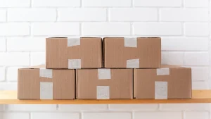 Fünf Pappkartons auf einem Holzregal vor einer weißen Ziegelwand, Beitragsbild zum Punktesammeln mit PAYBACK bei Amazon